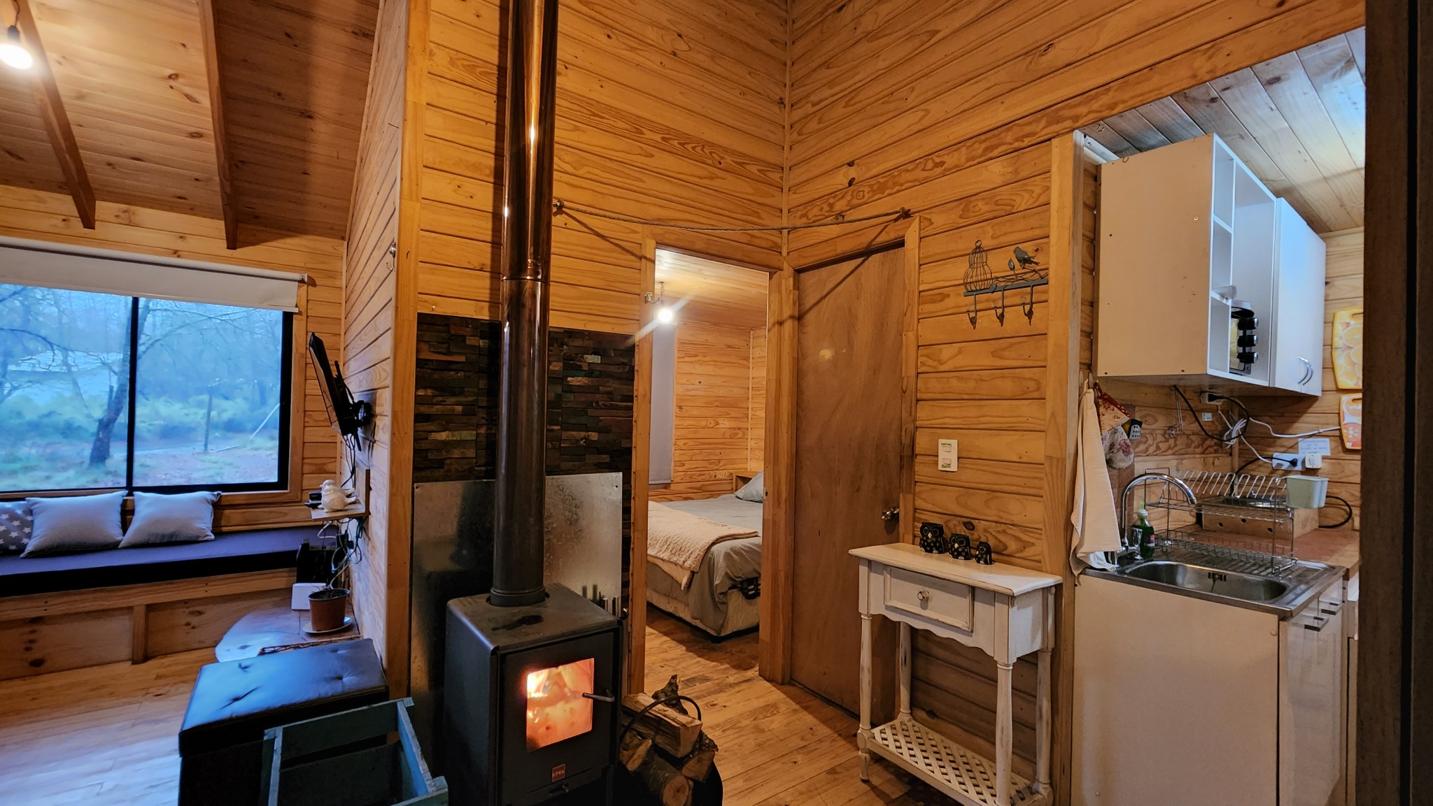 Interior de la cabaña con estufa, cocina y acceso al dormitorio